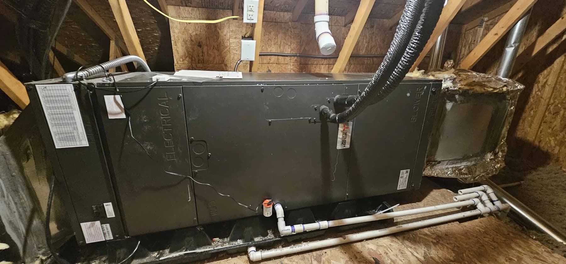 Horizontal indoor air handler between attic framing, with drain piping and insulated refrigerant lines visible