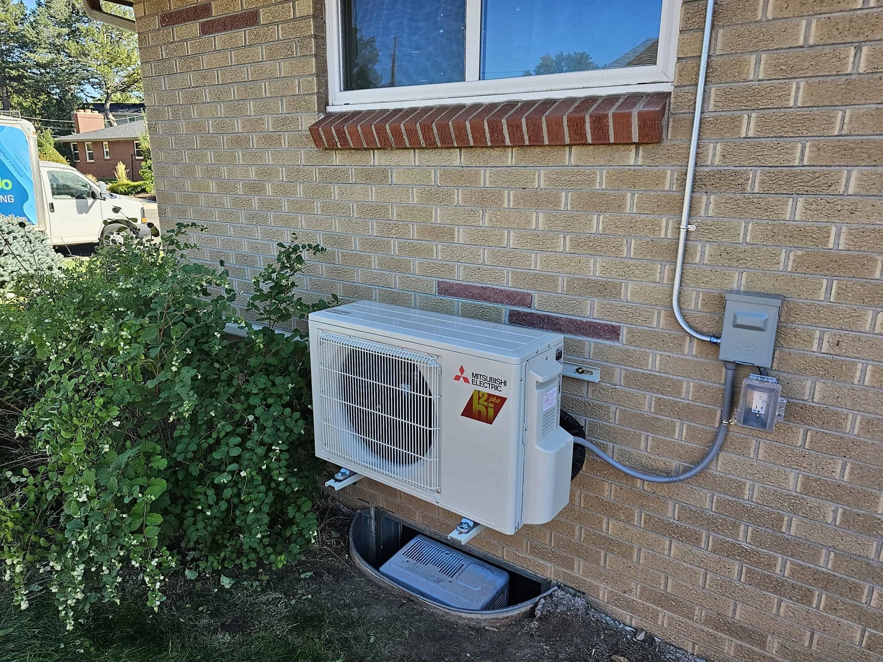 Outdoor Mitsubishi unit installed beside a brick wall with refrigerant and electrical connections
