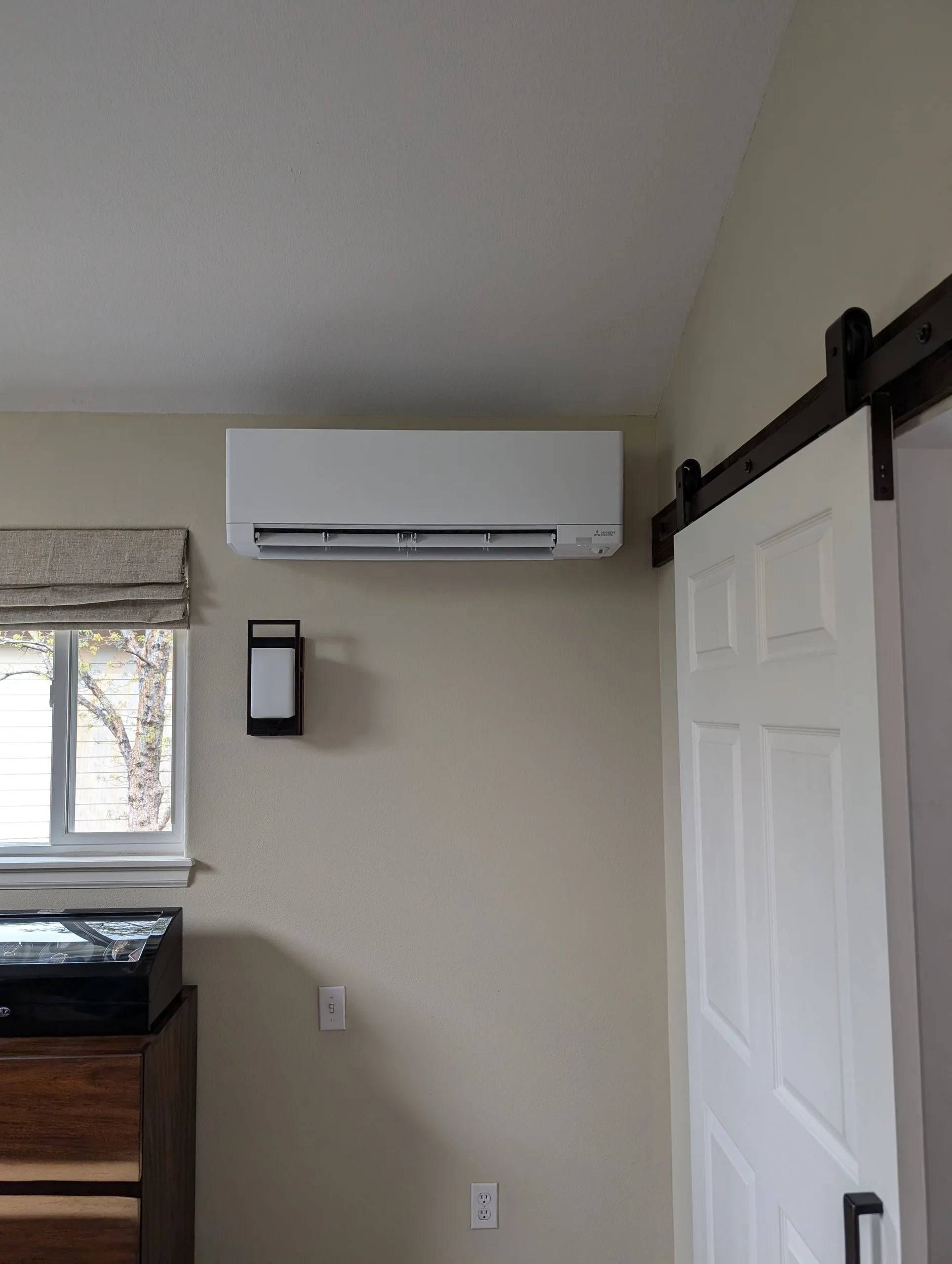 White wall-mounted indoor unit high on a bedroom wall beside a sliding white barn door