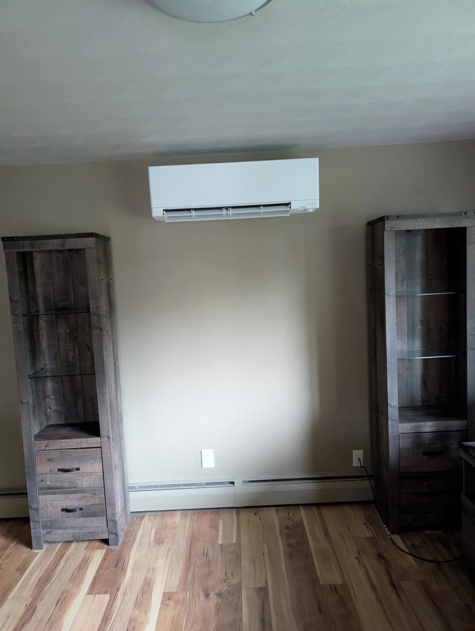 A ductless indoor unit high on a bedroom wall between two wood cabinets